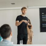 Young male professional giving a presentation to colleagues in a modern office setting.